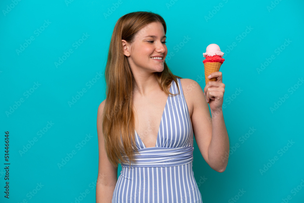 Young caucasian woman in swimsuit eating ice cream isolated on blue background with happy expression Young caucasian woman in swimsuit eating ice cream isolated on blue background with happy expression