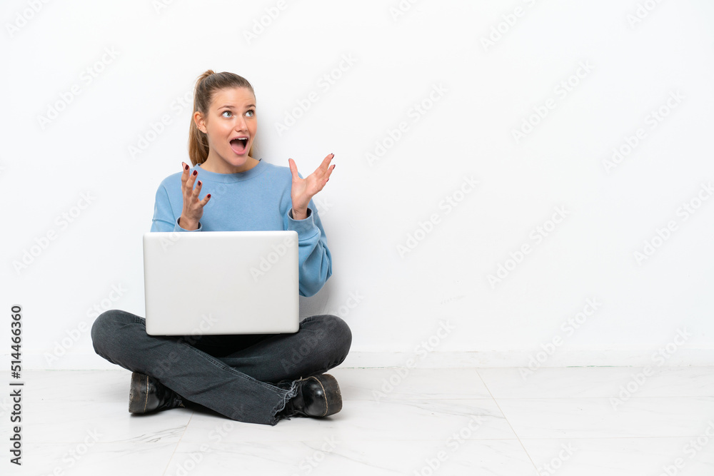 Young woman with a laptop sitting on the floor with surprise facial expression Young woman with a laptop sitting on the floor with surprise facial expression