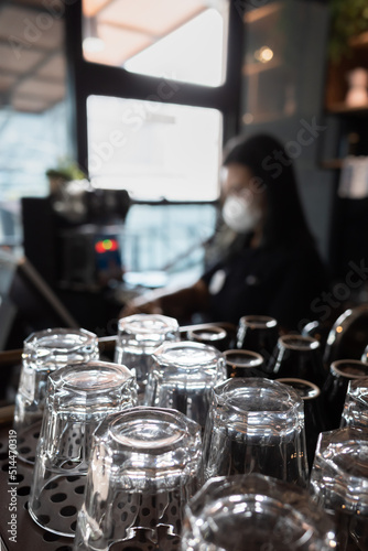 An Array of Clean Glasses in a Coffee Shop with a Female Cashier on the Background