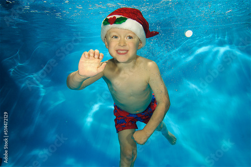 Child under water waving at camera whilst wearing a Santa hat