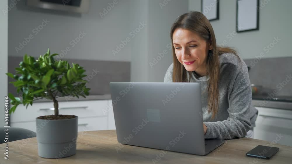Woman standing in home cozy kitchen use laptop do freelance work, chatting with someone, answering e-mail. Concept of remote work. Woman standing in home cozy kitchen use laptop do freelance work, chatting with someone, answering e-mail. Concept of remote work.