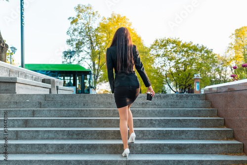 Fotografi Business woman walking,climb on the stairs holding paper coffee cup,rear view