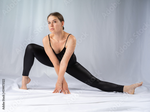 sports girl. Studio. Sports girl doing stretching exercises. Photo of a European girl in black sportswear on a gray background. Strength and motivation