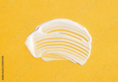 The texture of white cream on yellow background. A smear of moisturizer closeup. Lotion swatch. Beauty, skin care product smear smudge drop. SPF sunscreen cream sample