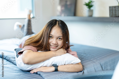 A cute long-haired Asian teenage girl hugging a pillow in bed in her bedroom with a happy smile on her face.