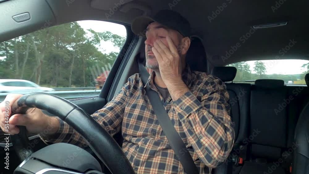 A tired driver rubs his eyes and blinks while driving on a busy highway. A tired driver rubs his eyes and blinks while driving on a busy highway.