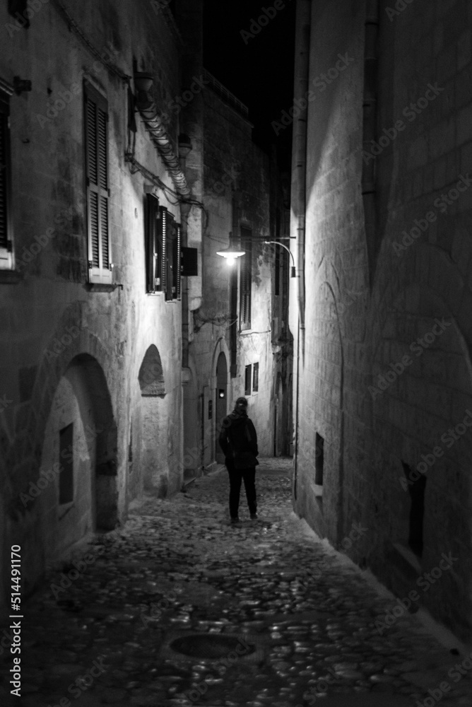 Obraz premium A person walking through a narrow alley at night, Italy