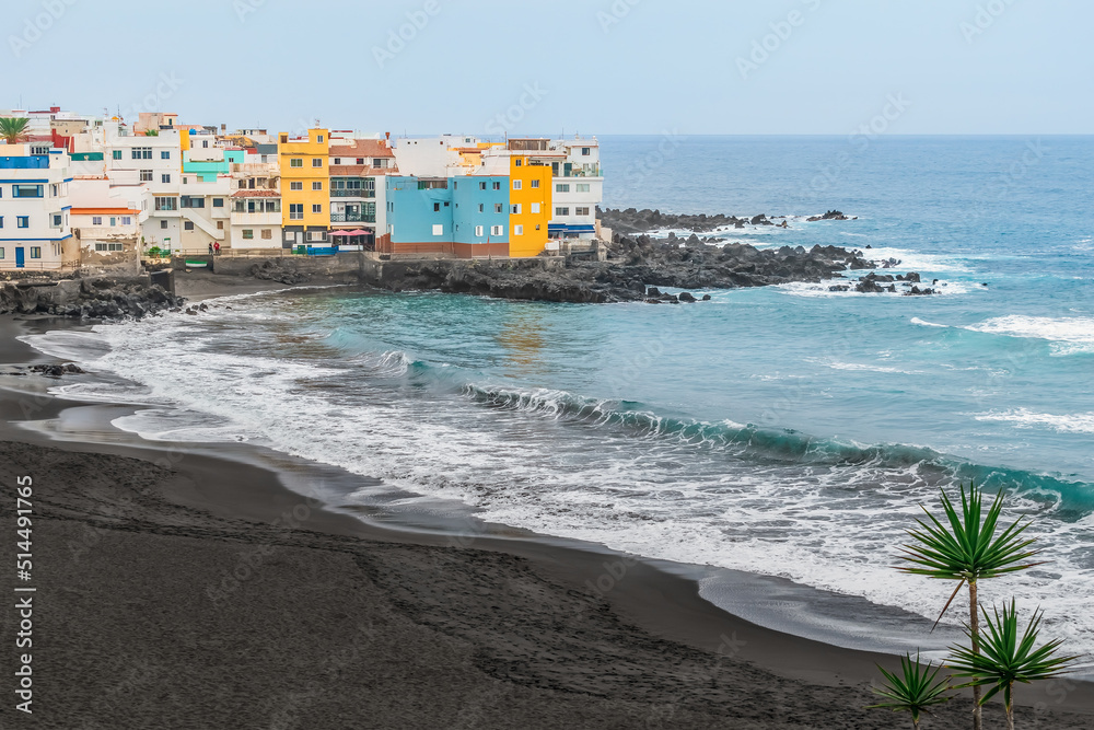 Playa Maria Jimenez beach with black sand in Puerto de la Cruz, Spain. Coastline of the Atlantic Ocean with bright color buildings among the rocks and big waves during a storm, no people