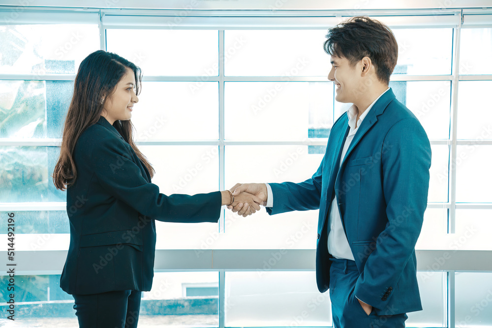 Business people shaking hands. Young modern man and women in smart casual wear shaking hands while standing in the office on windows background.