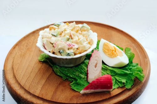 Salad with crab sticks, cubed cucumber, corn and egg with mayonnaise on a board.