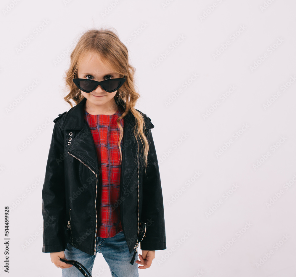Funny little girl in a leather jacket and sunglasses listens to rock music on the white background Funny little girl in a leather jacket and sunglasses listens to rock music on the white background