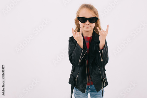 Funny little girl in leather jacket and sunglasses listening to rock music and showing fingers