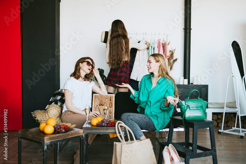 three young woman female caucasian students at swap party try on clothes, bags, shoes and accessories, change clothes with each other, second hand for things, zero waste life, eco-friendly