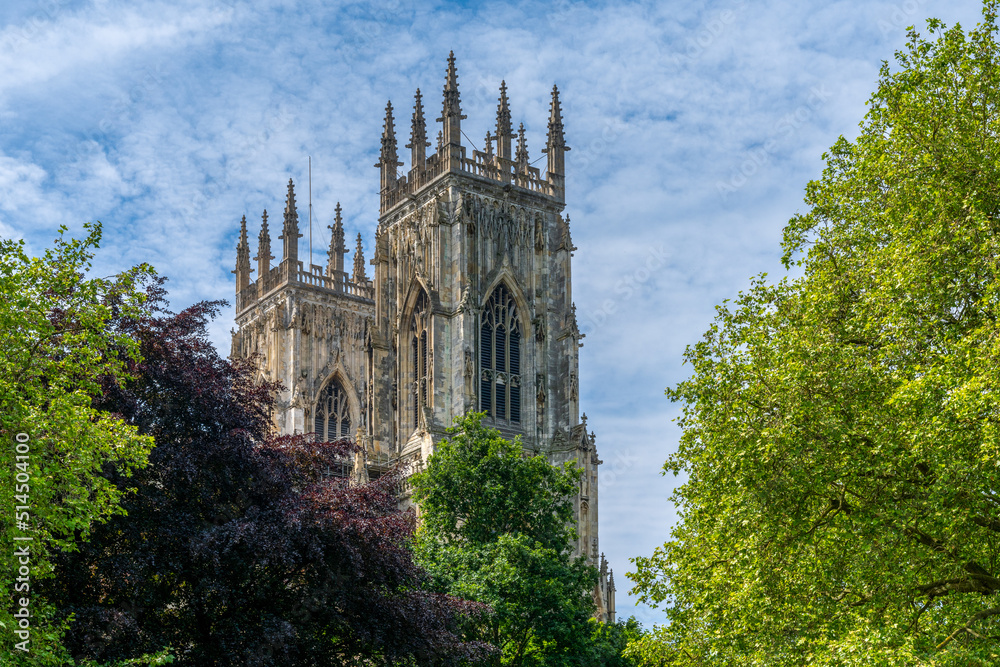 close-up view of the bell towers of the York Minster surrounded by colorful summer trees under a blue sky