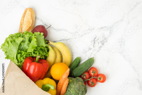 Grocery brown paper bag full of fresh fruits and vegetables on white marble background. Shopping and delivery service concept. Healthy food diet concept. Free space. Flat lay