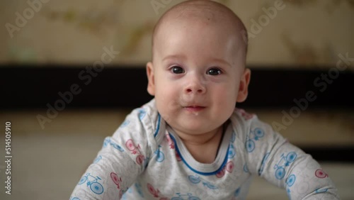 Newborn Active Baby Cute Smiling Teethless Face Portrait Early Days On Stomach Developing Neck Control. 5 Months Child On White Bed Looking on Camera. Infant, Childbirth, Parenthood, Beginning Concept photo