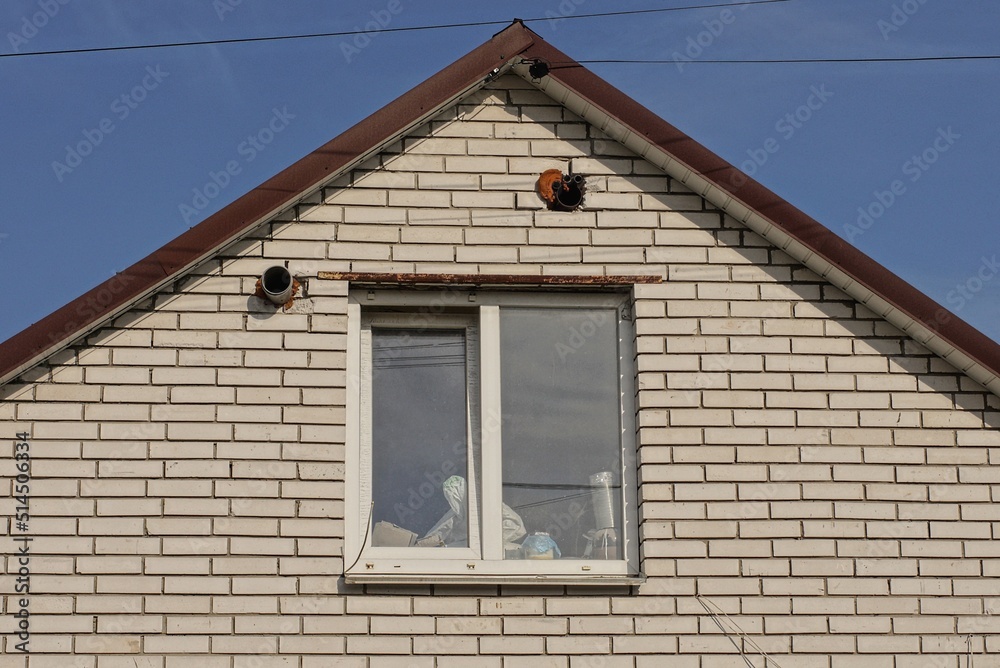 white brick attic of a private house with one window against a blue sky