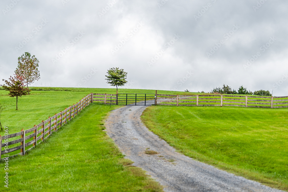 Farm rural countryside with fence in Rockbridge County in Buena Vista, Virginia during fall season with cloudy day and dirt road driveway on hill