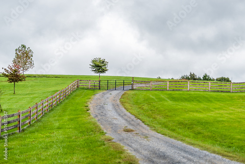 Farm rural countryside with fence in Rockbridge County in Buena Vista, Virginia during fall season with cloudy day and dirt road driveway on hill photo