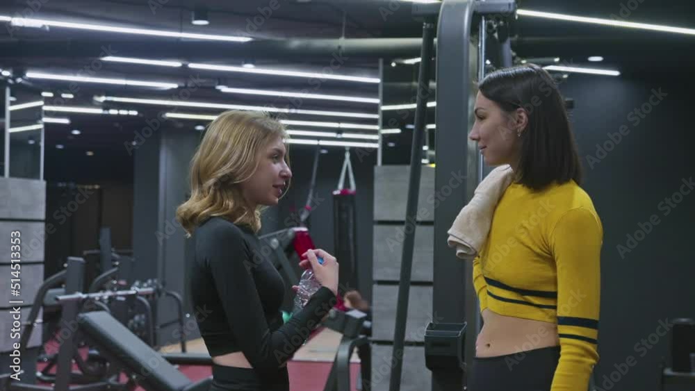 Two young women talk at gym. Blonde and brunette women say goodbye and leave Two young women talk at gym. Blonde and brunette women say goodbye and leave