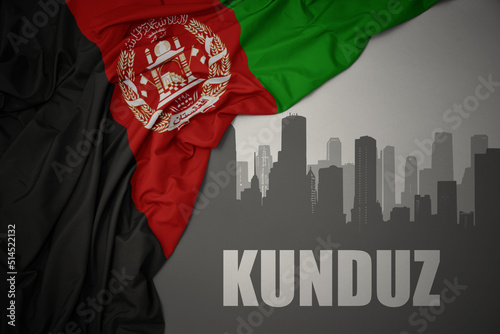 abstract silhouette of the city with text Kunduz near waving national flag of afghanistan on a gray background. photo