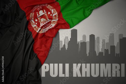 abstract silhouette of the city with text Puli Khumri near waving national flag of afghanistan on a gray background. photo