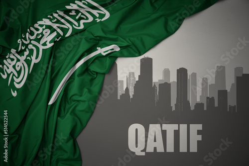 abstract silhouette of the city with text Qatif near waving national flag of saudi arabia on a gray background. photo