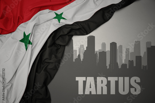 abstract silhouette of the city with text Tartus near waving national flag of syria on a gray background. photo