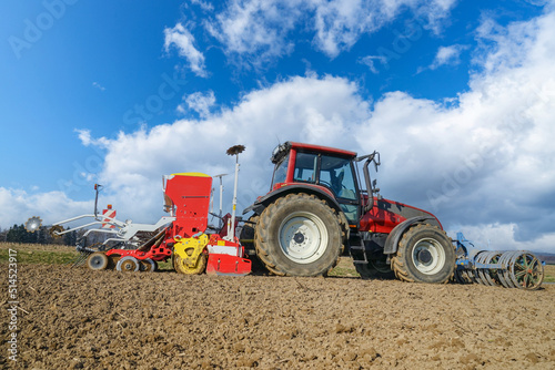 Agrarmotive - Frühjahrsbestellung. Landwirt mit rotem Schlepper und roter Drillmaschine bei der Aussaat von Sommergetreide in hügeliger Landschaft. 