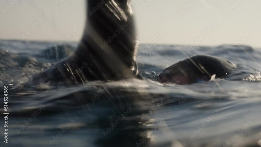 Man swimming front crawl in open water swimming underwater view. Sportsman in goggles and cap training close up tracking shot. Professional muscular male swimmer workout