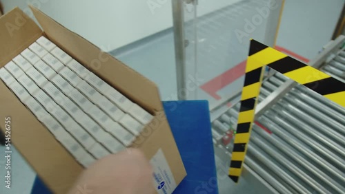 A pharmaceutical production worker takes the box with a packaged batch of medicine from the assembly line and packs it.