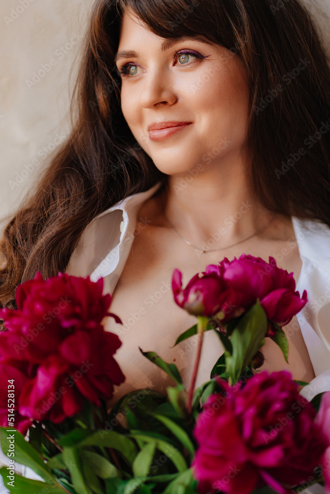a beautiful young brunette woman in a white shirt with a bouquet of peonies. a beautiful young brunette woman in a white shirt with a bouquet of peonies.