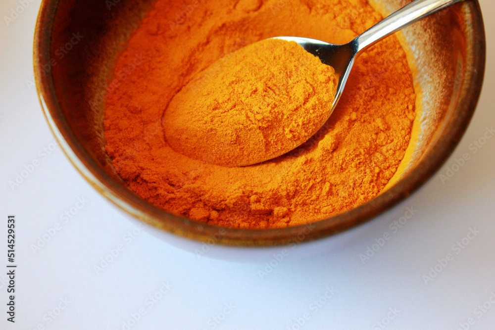 Fototapeta premium yellow turmeric powder in a brown bowl with a spoon on white background, turmeric powder as ingredient for cooking