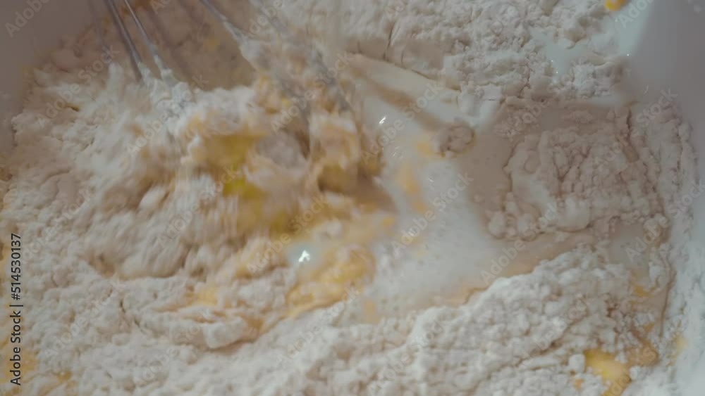 The process of preparing liquid dough for pancakes, stirring the mixture with a whisk for further preparation. Adding flour The process of preparing liquid dough for pancakes, stirring the mixture with a whisk for further preparation. Adding flour