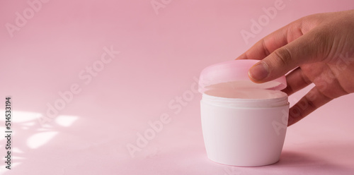 Hand opening a skin cream bottle for women on pink background