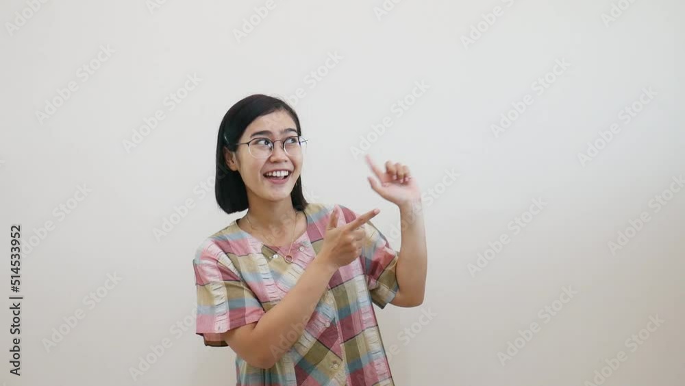 Happy asian woman standing while pointing empty space. Isolated on white wall with copyspace Happy asian woman standing while pointing empty space. Isolated on white wall with copyspace