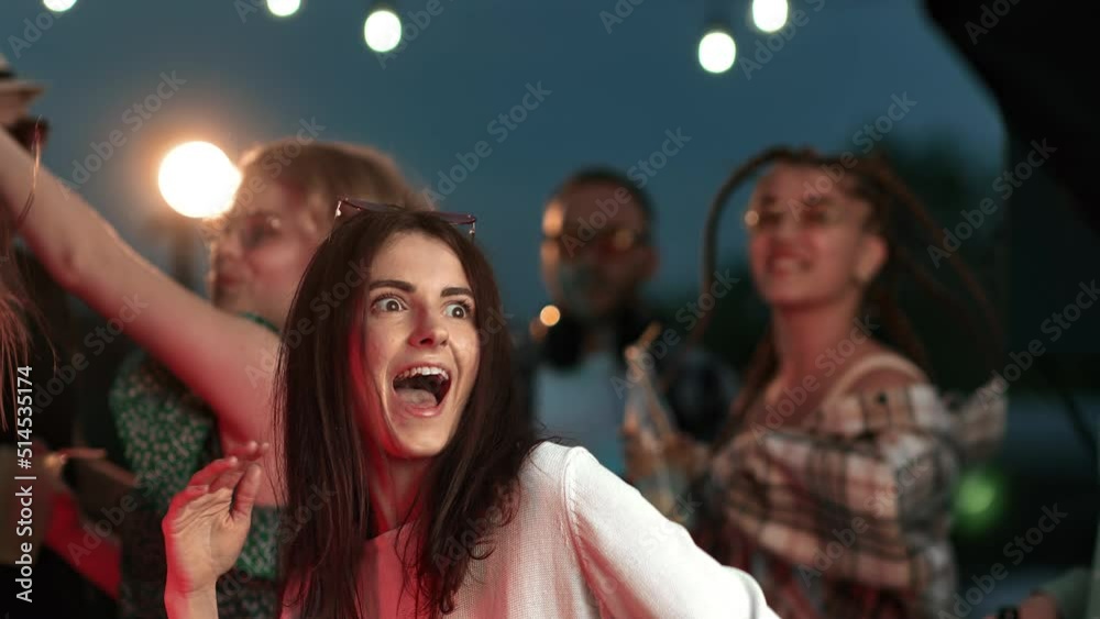 Portrait happy brunette curly woman dancing at night clubbing roof party with people friends crowd