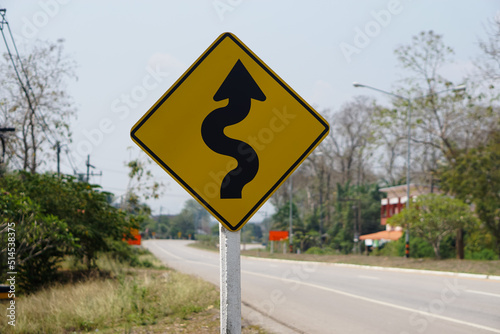 Yellow traffic sign with twisty arrow symbol at rural road Thailand to warn drivers be careful when driving on twisty way road. Concept : Warning traffic sign for transportation. 