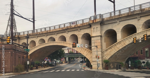 Arched Bridge Extending OVer Black Top Streets with Cars and Stores