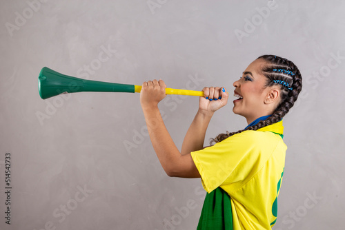 Young brazilian cheerleader with a vuvuzela on grey background celebrating