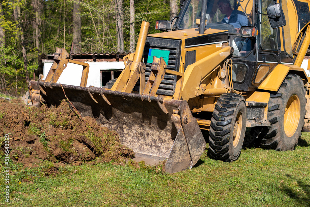 Clearing and leveling a private land plot. Yellow excavator driving earth in a wide bucket