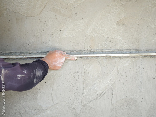 Plasterer using screeder smoothing putty plaster mortar on wall. house building concept. photo