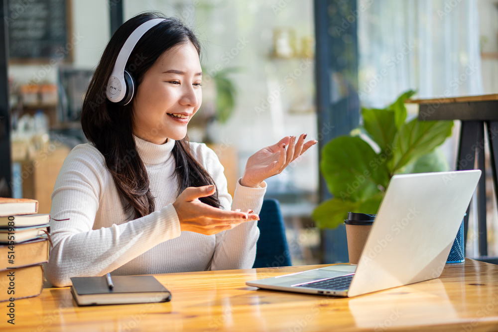 Cheerful and beautiful Asian woman wearing headphones and looking at digital tablet in video conferencing and online classes on the Internet at a coffee shop. Cheerful and beautiful Asian woman wearing headphones and looking at digital tablet in video conferencing and online classes on the Internet at a coffee shop.