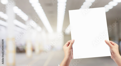 Hands holding white empty paper at factory production background.