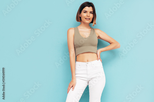 Young beautiful smiling female in trendy summer jeans clothes. Carefree woman posing near blue wall in studio. Sexy positive model having fun indoors. Cheerful and happy. Isolated