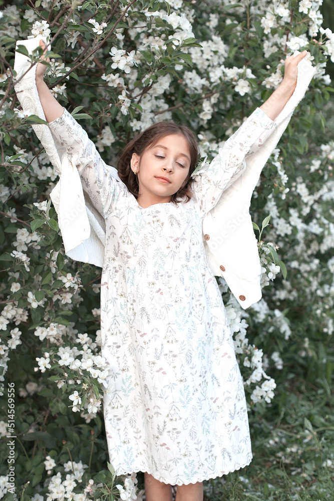 A beautiful little girl among the green foliage and white flowers of blooming apple trees. Spring day. A happy child smiles and looks at the camera A beautiful little girl among the green foliage and white flowers of blooming apple trees. Spring day. A happy child smiles and looks at the camera