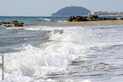 Beach on the Italian Riviera with sun, sea and stones in the sea water. Rough Sea and Foamy Waves on Shore at Mediterranean Coast in Sunrise