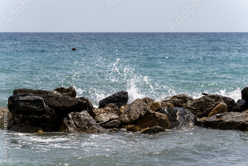 Beach on the Italian Riviera with sun, sea and stones in the sea water. Rough Sea and Foamy Waves on Shore at Mediterranean Coast in Sunrise