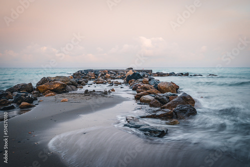 Beach on the Italian Riviera with sun, sea and stones in the sea water. Rough Sea and Foamy Waves on Shore at Mediterranean Coast in Sunrise