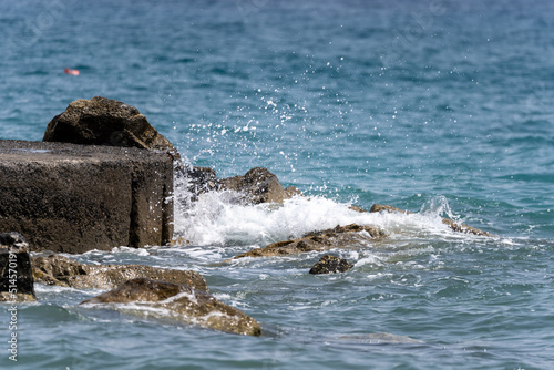 Beach on the Italian Riviera with sun, sea and stones in the sea water. Rough Sea and Foamy Waves on Shore at Mediterranean Coast in Sunrise